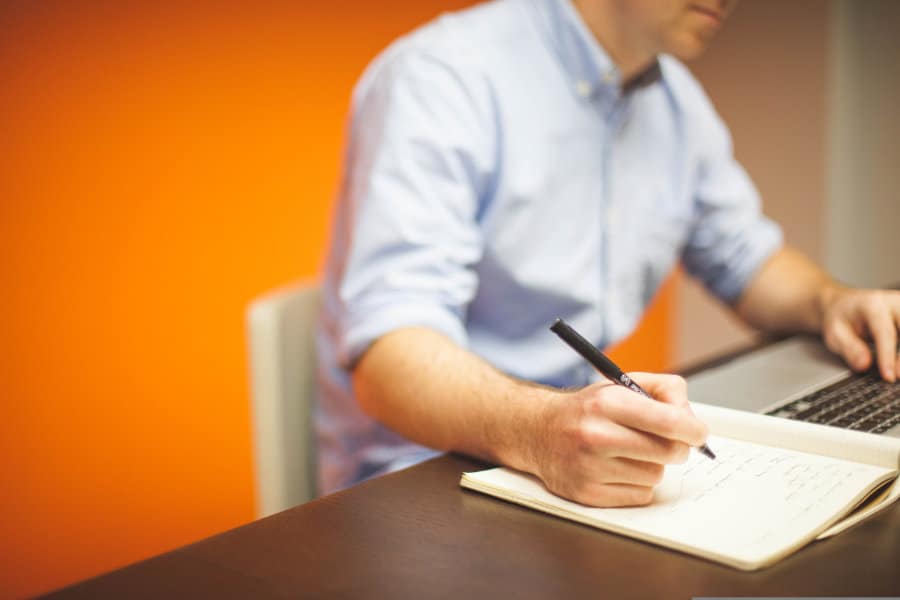 Man writing in a notebook, working next to a laptop