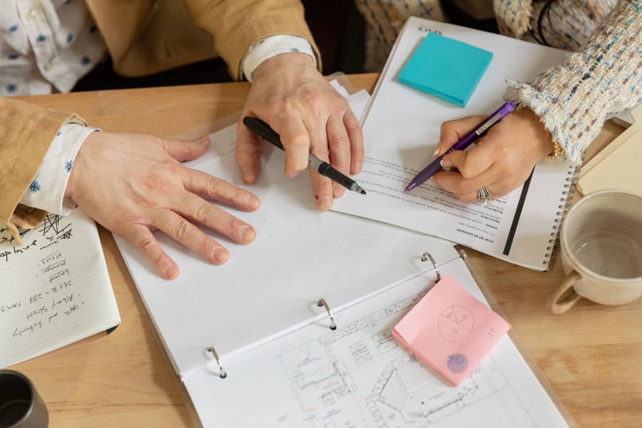 Two people working together through notes in some notebooks